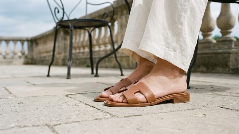 Brown leather Hermès Oran sandals paired with cream linen pants on an outdoor stone terrace