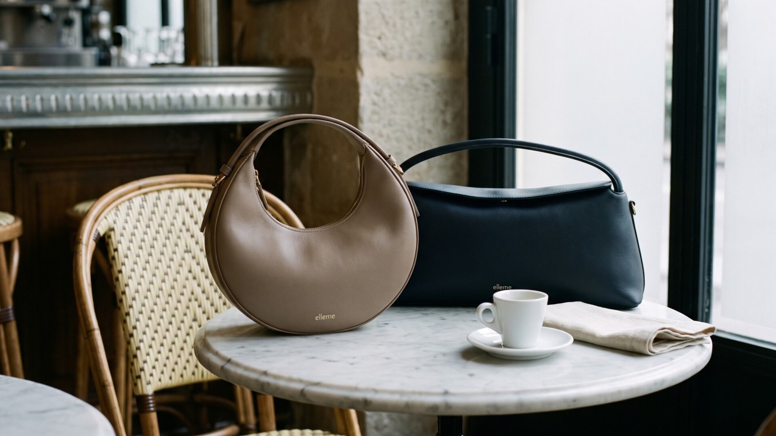 Elleme Boomerang and Le Bateau leather handbags resting on a marble Parisian bistro table