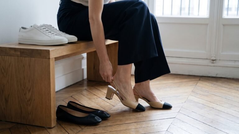 Woman putting on two-tone slingback heels beside black ballet flats and white leather sneakers