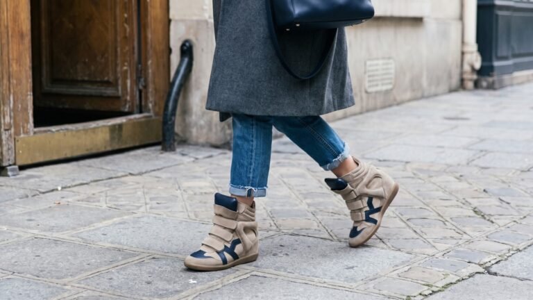 Woman walking on a stone sidewalk wearing beige and blue Isabel Marant Bekett wedge sneakers and cropped jeans