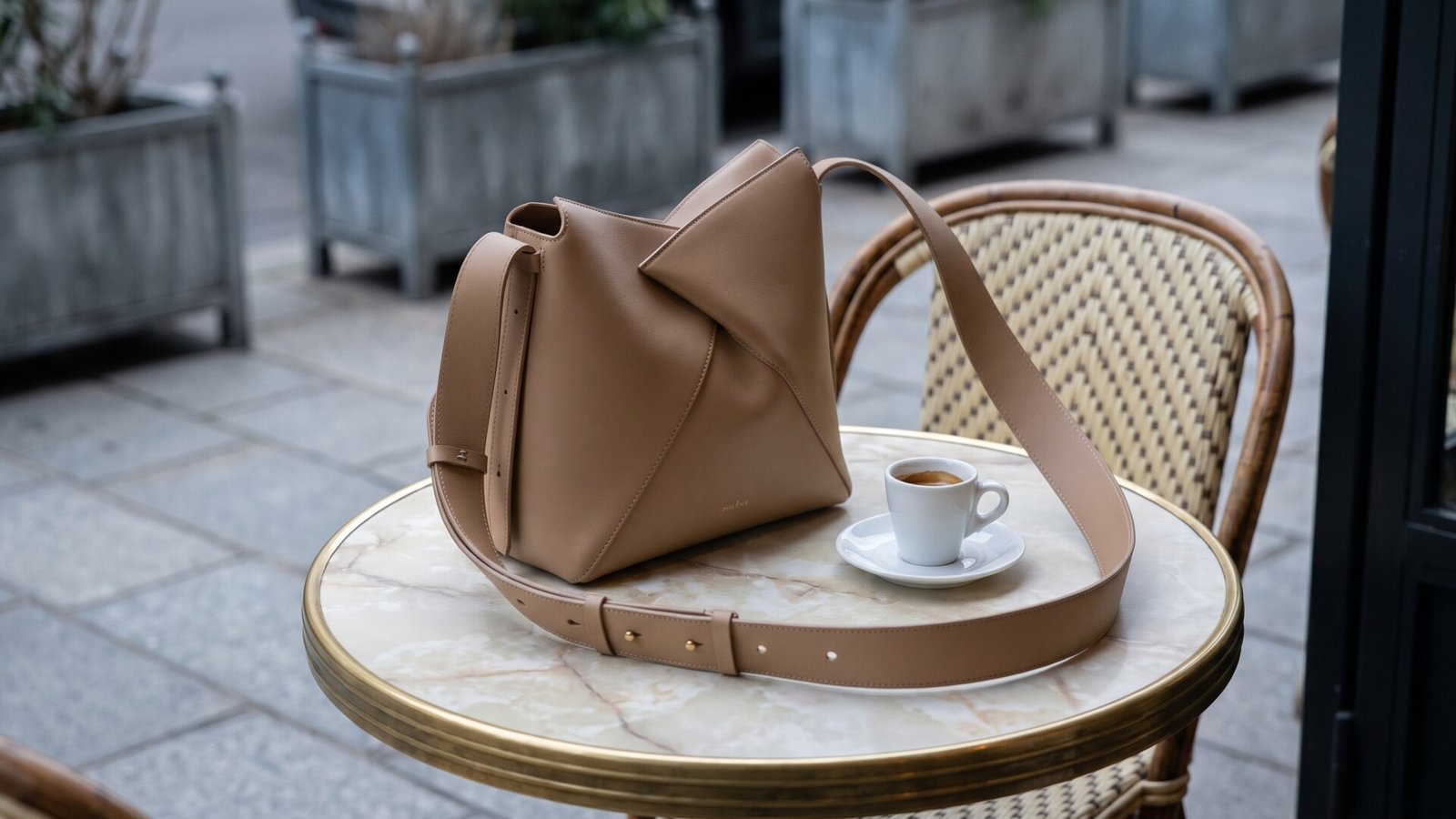 Beige sculptural Polène leather handbag beside an espresso cup on an outdoor marble café table