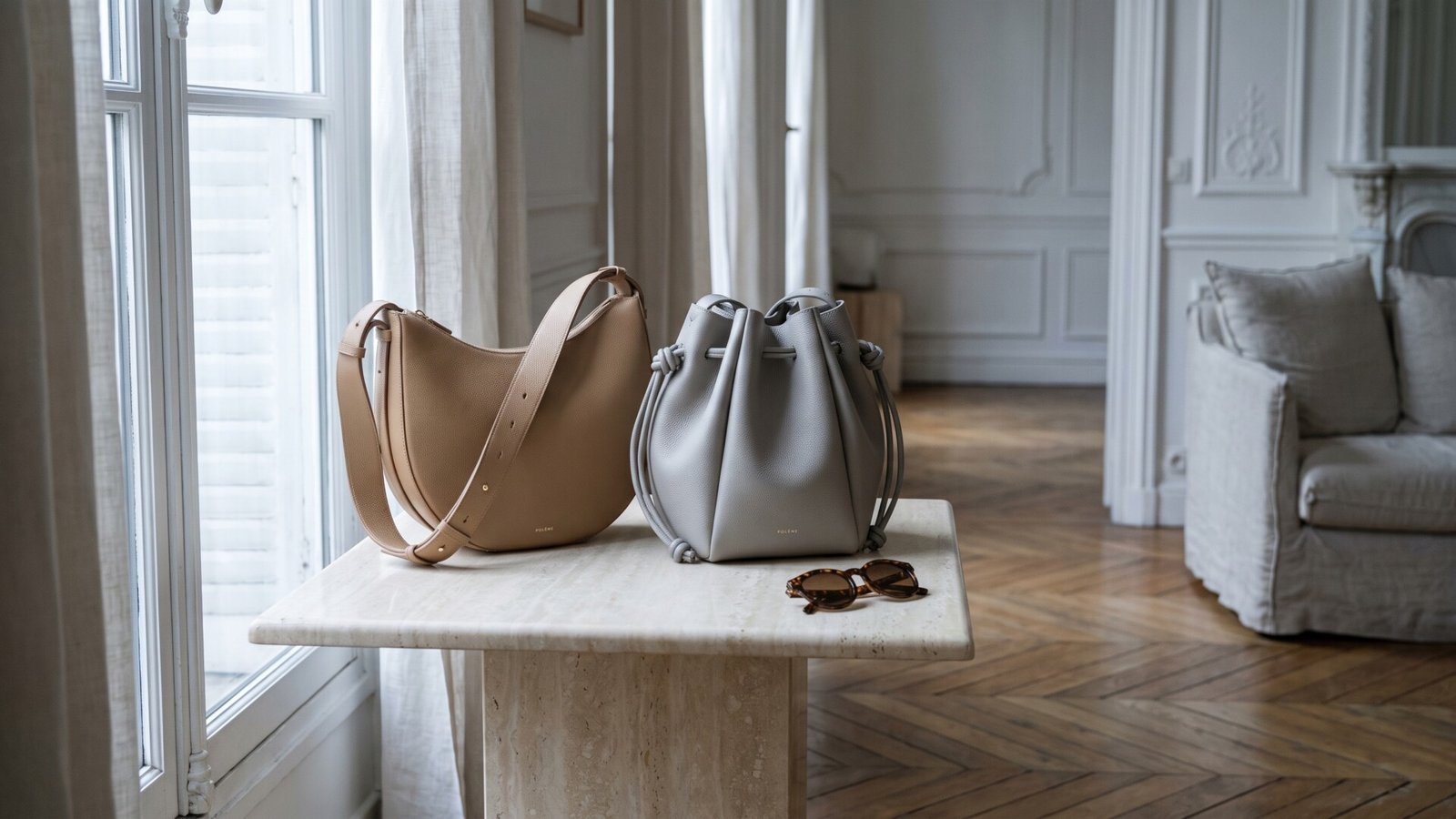 Polène Numéro Dix shoulder bag and Numéro Huit bucket bag resting side by side on a marble pedestal table