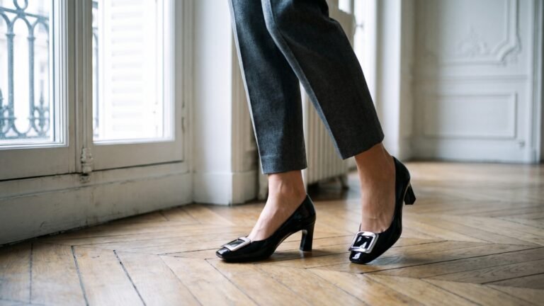 Black patent Roger Vivier Belle Vivier buckle pumps paired with cropped tailored trousers on parquet flooring