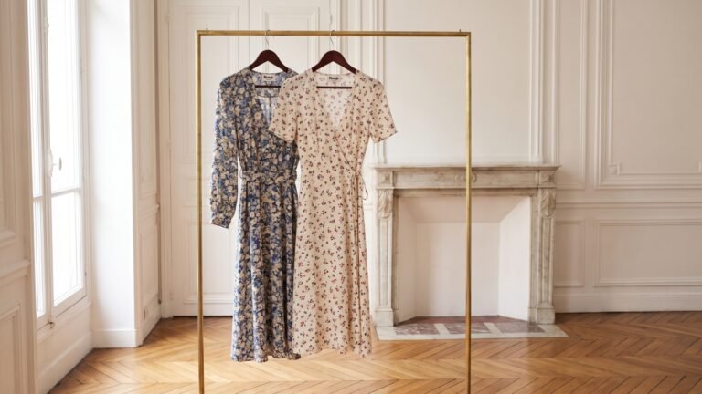Two Rouje floral dresses hanging on a brass rack inside an elegant Parisian apartment room