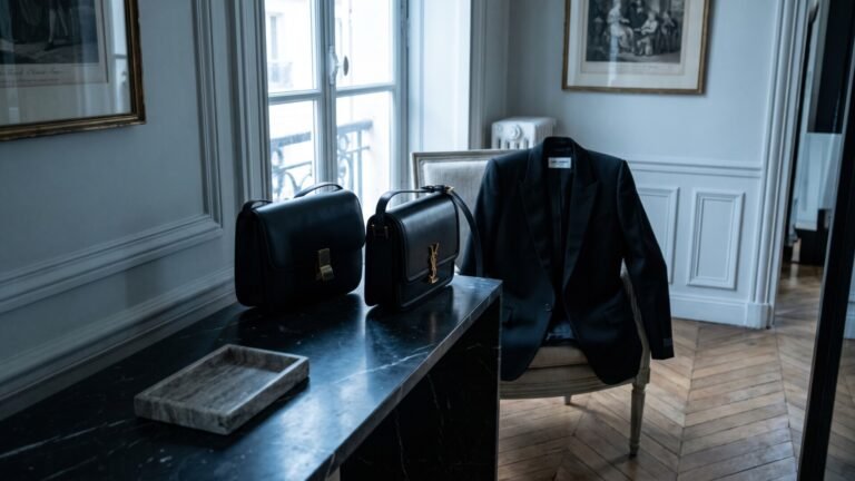 Black Celine Box bag and Saint Laurent monogram handbag on a dark marble table beside a tailored black blazer
