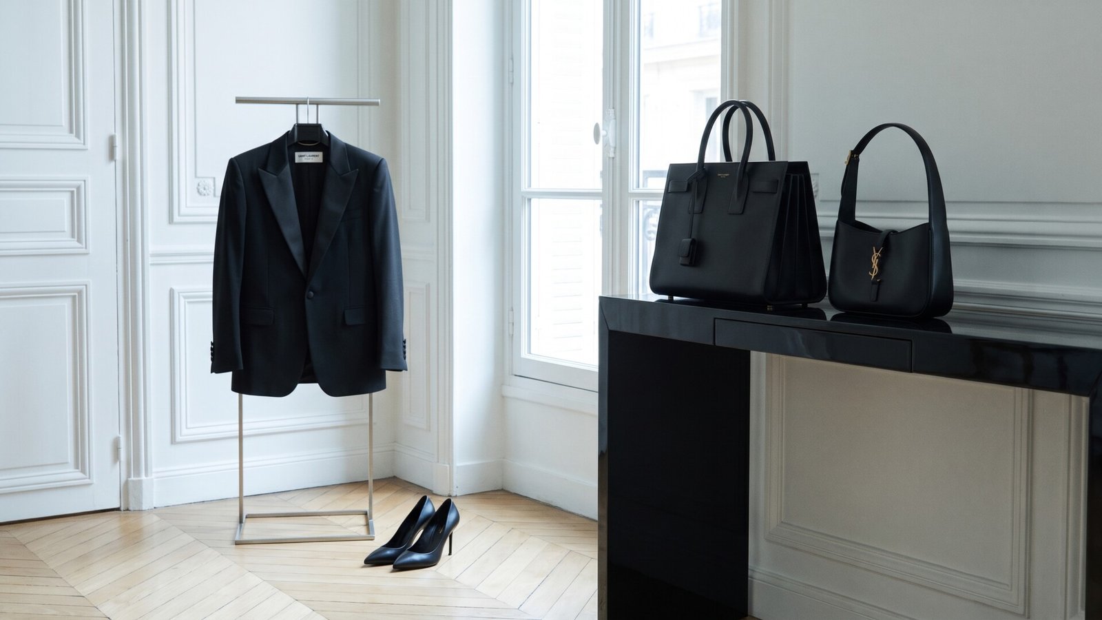 Black Saint Laurent tuxedo jacket on a rack beside matching pumps and contemporary leather handbags